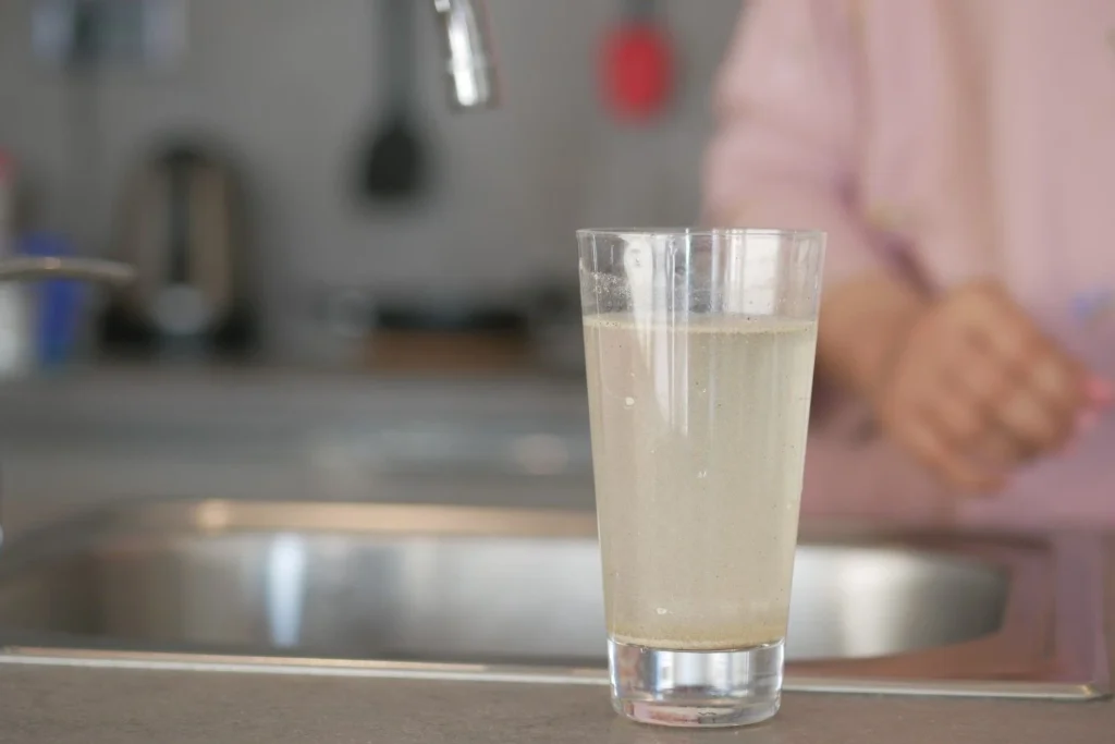 Cloudy tap water in a glass showing mineral buildup from hard water