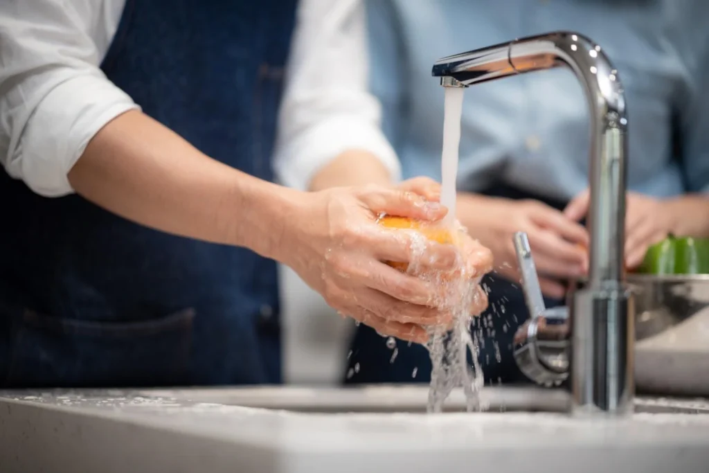Person washing fruit under a kitchen tap, illustrating how hard water is commonly used in everyday household activities.