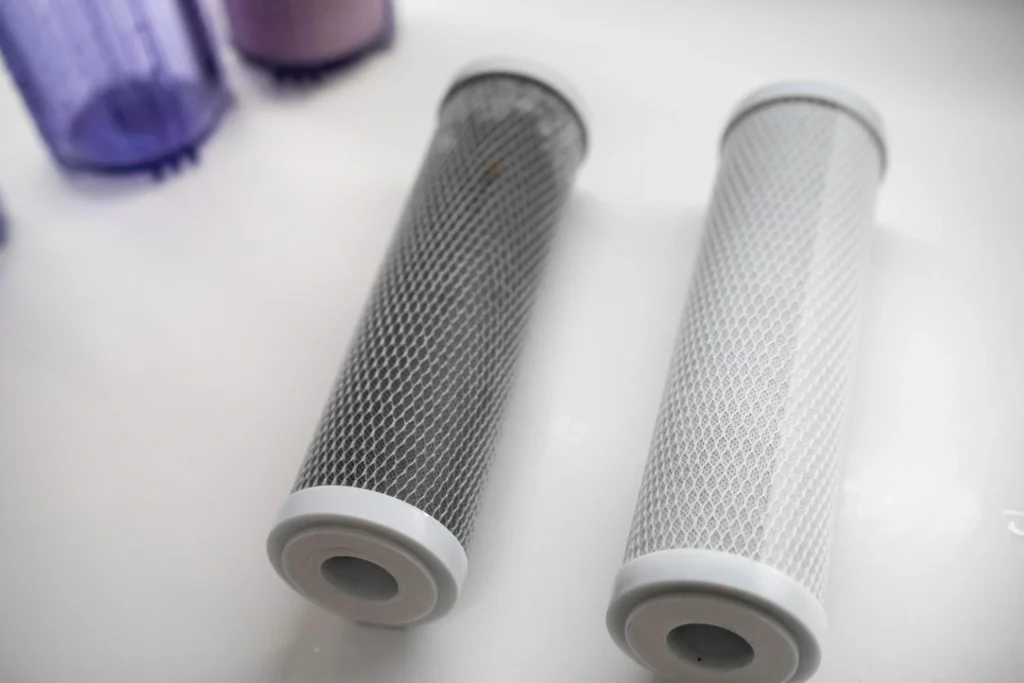 A side-by-side comparison explaining what is activated carbon filtration by showing a used, dark-grey carbon block filter next to a clean, white replacement filter.