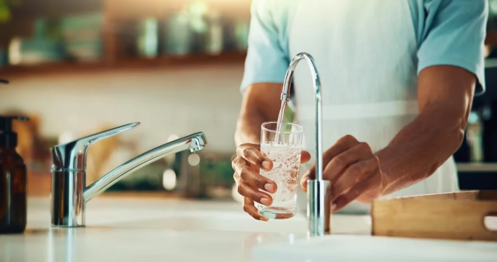 Person filling a glass with clean tap water in a kitchen after installing a whole house water softener for hard water